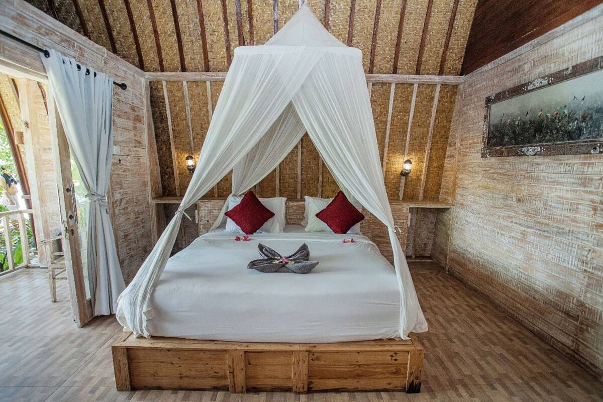 A room with a wooden bed, white canopy, red pillows, and a painting on the wall.