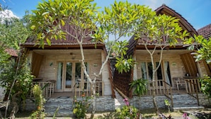 Una casa de madera con tejado de baldosas, rodeada de abundante vegetación y un camino de piedra.