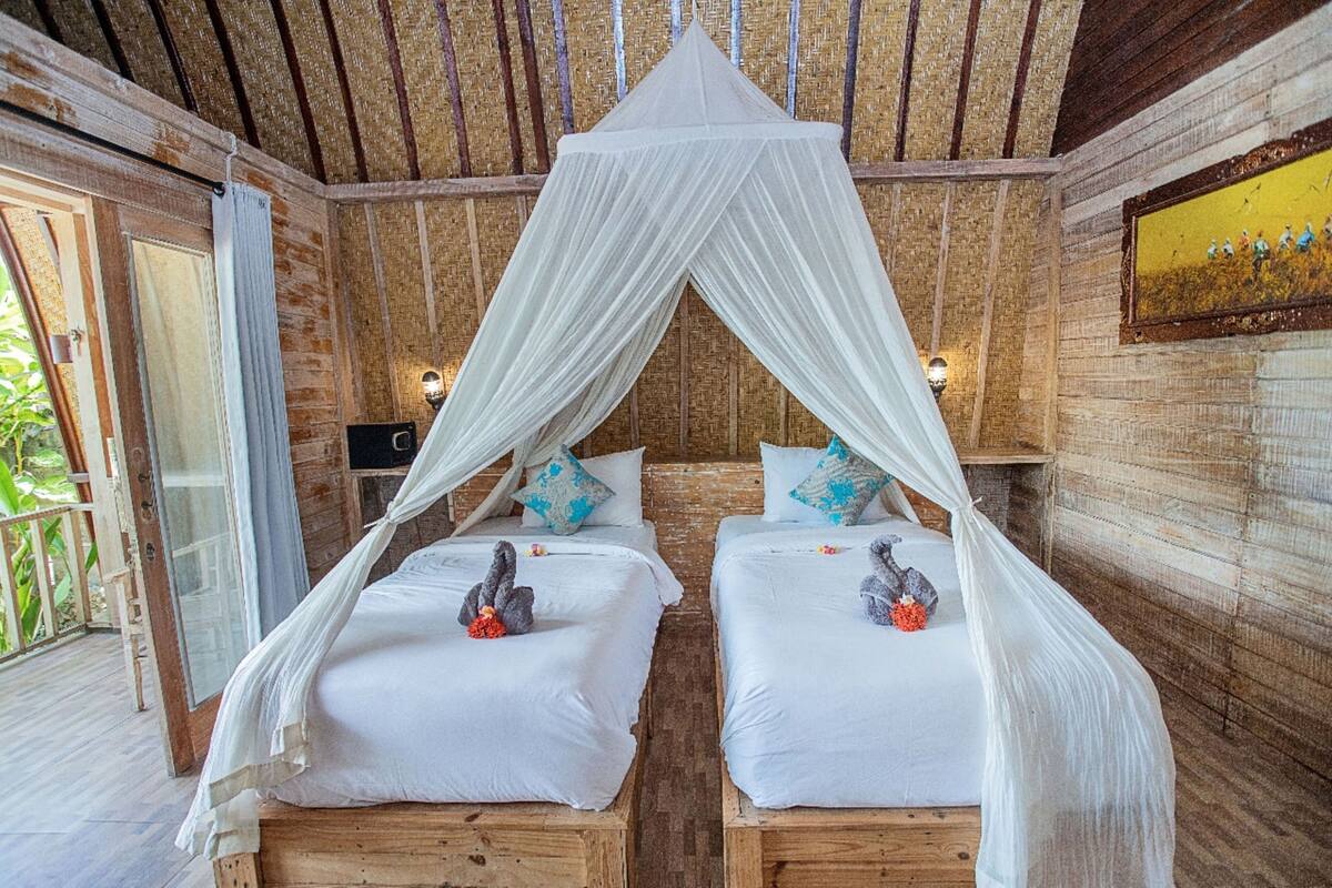 A room with two wooden beds, white bedding, and a canopy bed. There are decorative pillows and a small table with a lamp.