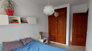 Une chambre à coucher avec un lit, une table de chevet, une plante en pot, une armoire et une porte.