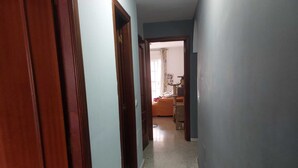 Un couloir étroit, avec des portes en bois d’un côté et une chambre visible au fond.