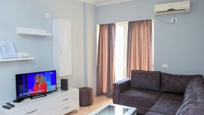 A living room with a flat-screen TV, a sofa, a coffee table, a cabinet, and a window with curtains.