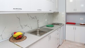 A kitchen with white cabinets, a marble backsplash, a stainless steel sink, and a fruit bowl on the counter.