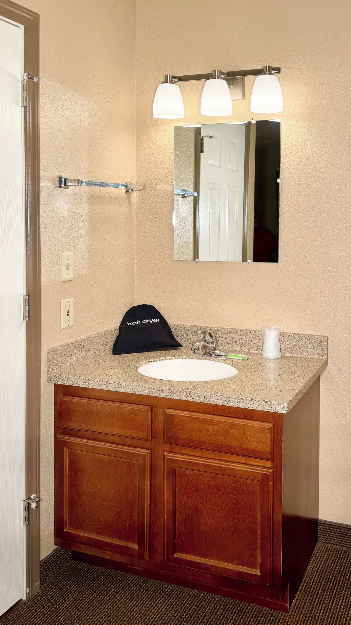 A bathroom with a granite countertop sink, wooden vanity, and a mirror with three lights.