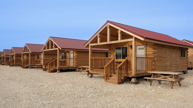 A row of wooden cabins with red roofs, wooden railings, and picnic tables. - Young's Motel (Tok)