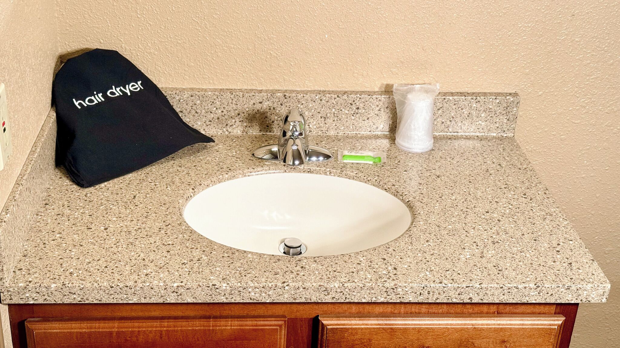 A bathroom sink with a faucet, a hair dryer, and a toothbrush on a granite countertop.