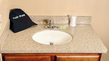 Un lavabo con grifo, un secador de pelo y un cepillo de dientes sobre una encimera de granito.