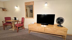 A hotel room with a wooden TV stand, a flat-screen TV, a desk with a telephone, two red chairs, and a wall-mounted mirror. - Young's Motel (Tok)