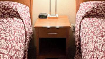 A hotel room with two beds, a nightstand with a lamp, and a painting of a mountainous landscape above the beds.