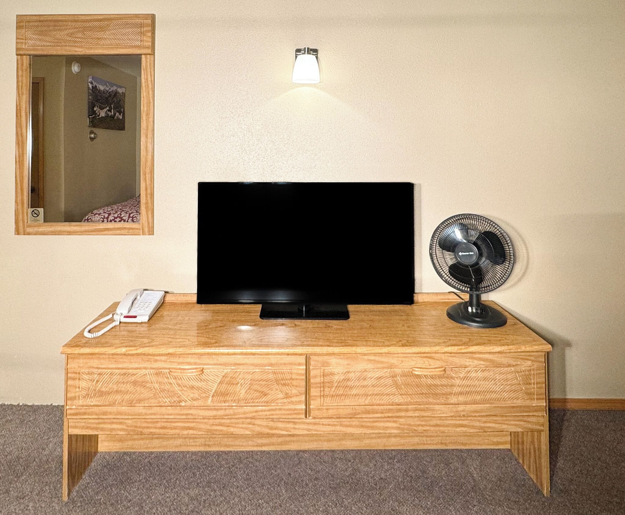A wooden TV stand with a flat-screen TV, a white telephone, and a standing fan.