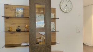 Un interior moderno con estantes de madera que exhiben objetos decorativos, un reloj de pared y un espejo que refleja una vista panorámica.