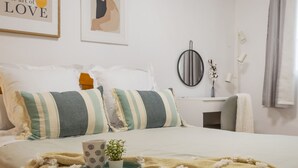 A neatly arranged bedroom with a bed, pillows, a bedside table, a mirror, and a wall art piece. - Bungalow PINK LAGOON (Torrevieja)
