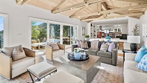 Ein großzügiger Wohnraum mit hohen Decken und großen Fenstern, eine gemütliche Sitzecke mit Sofas und einem Couchtisch sowie ein Blick ins Freie.