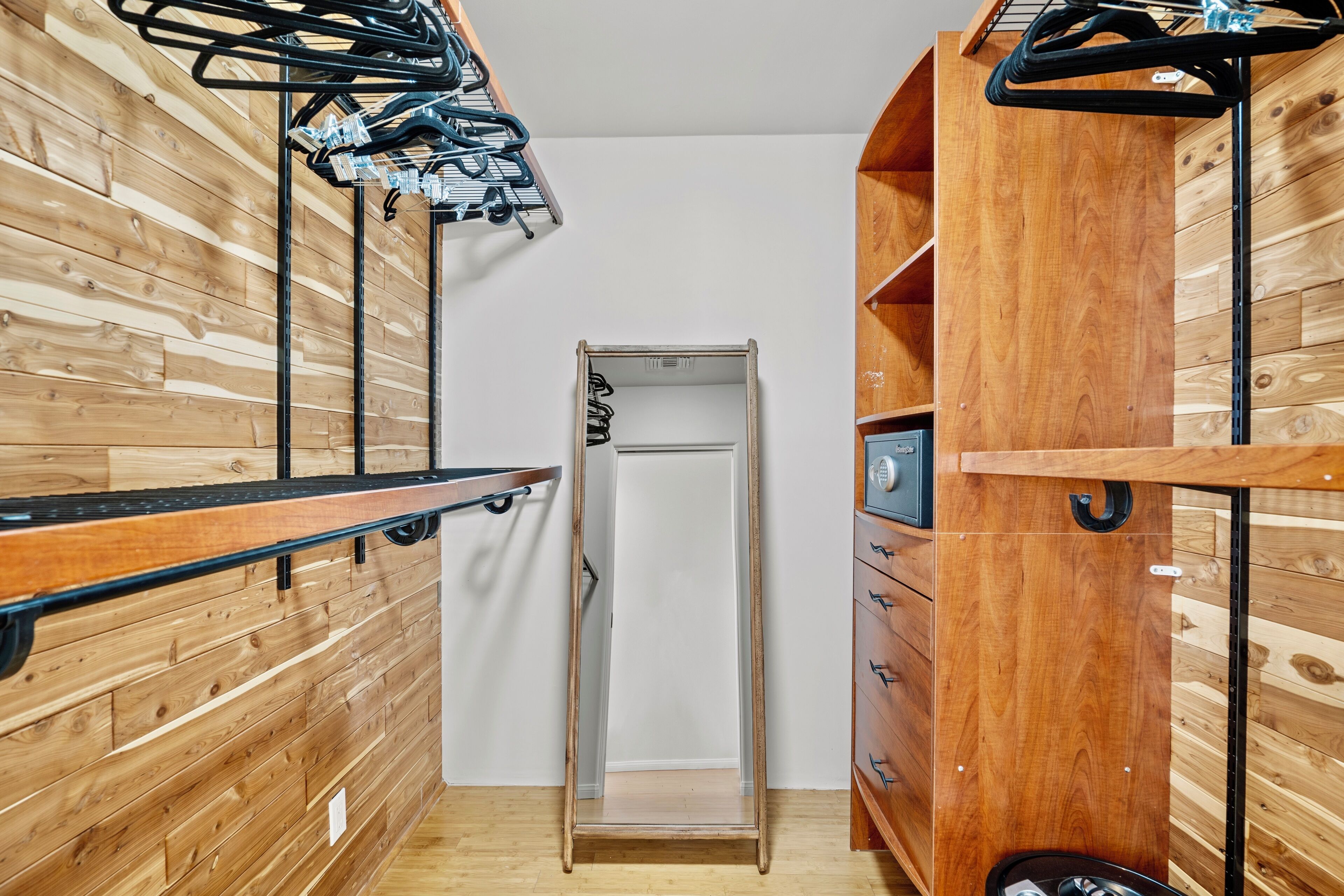 A narrow hallway with wooden walls, a metal rack with clothes, and a door leading to a room.