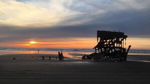 Uma praia com a silhueta de um grande naufrágio enferrujado ao pôr do sol.