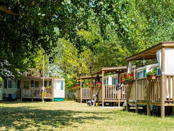 A row of mobile homes with wooden decks and flower boxes, surrounded by lush greenery.