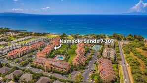 An aerial view of Kamaole Sands 7-307, featuring a coastal resort with multiple buildings, a swimming pool, and a clear view of the ocean. - Remodeled Condo Across Beach w Pool AC - Kamaole Sands 7307 (Kihei)
