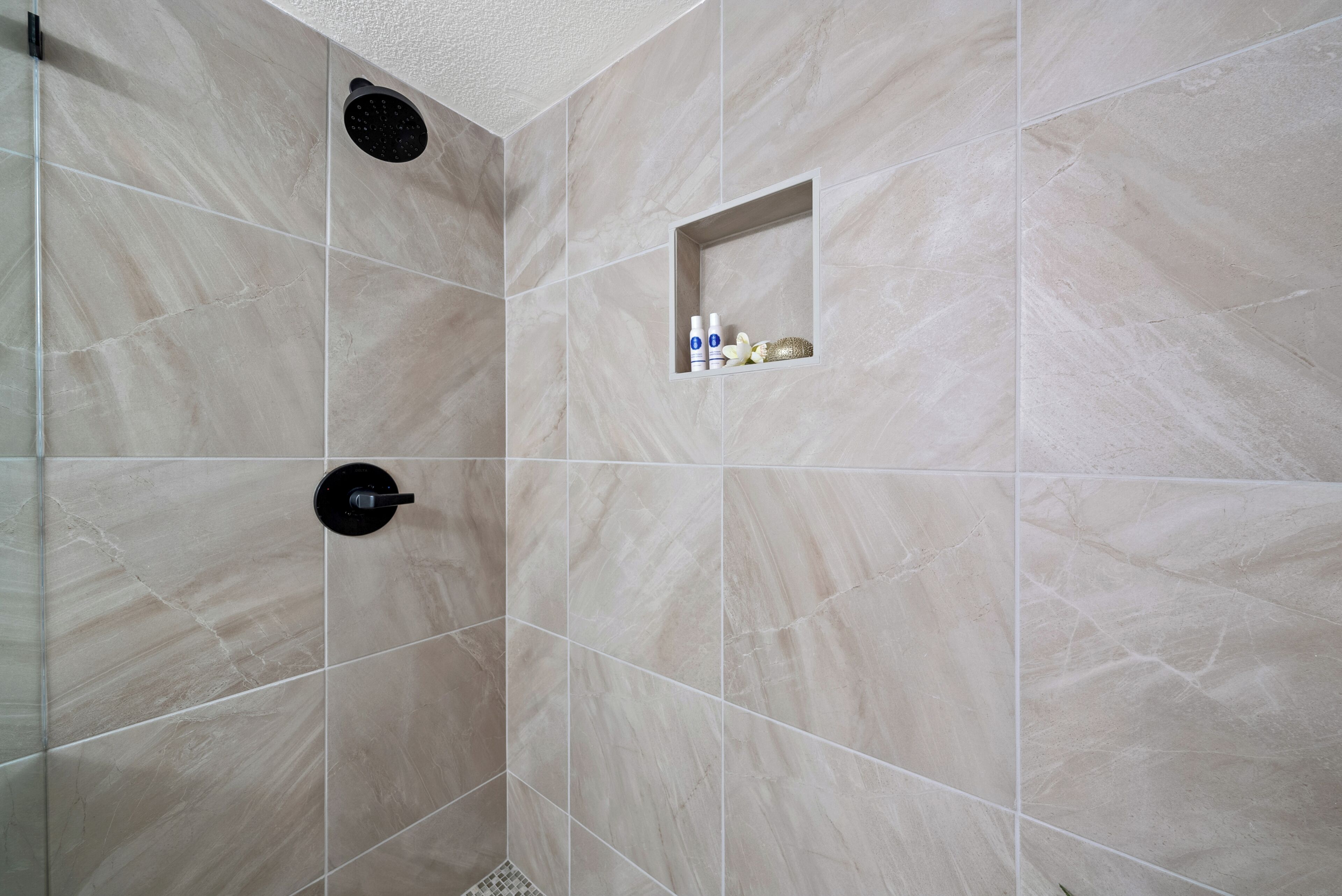 A shower area with a built-in shelf containing toiletries.