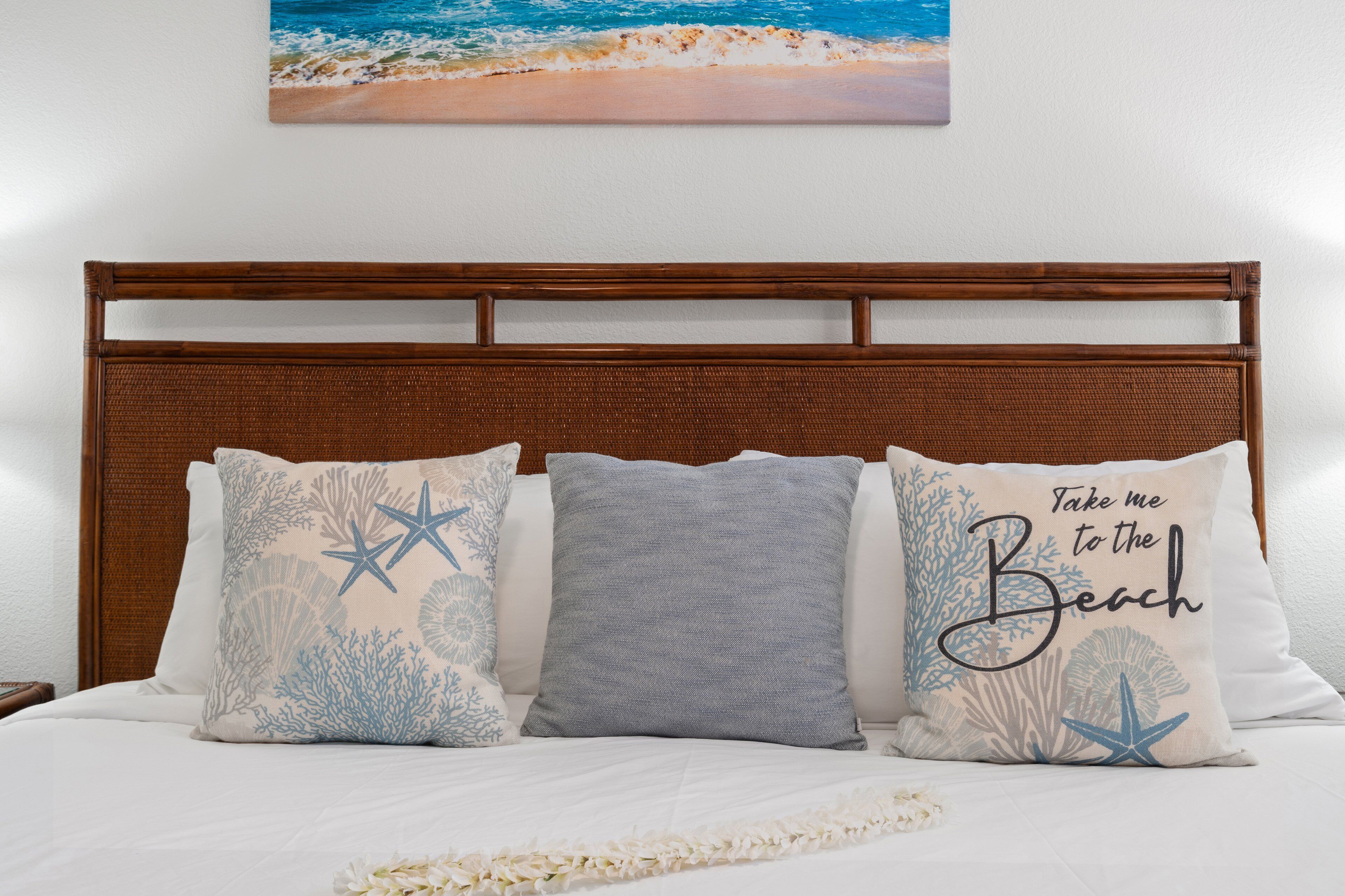 Ein Bett mit drei Kissen, einem hölzernen Kopfteil und einem Meeresmotiv an der Wand.