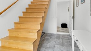 Un escalier en bois menant à une porte, un mur blanc orné de tableaux encadrés et un pouf noir.