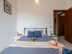 Una cama bien hecha con un edredón a rayas, una mesita de noche con libros, una planta pequeña y un sombrero de paja sobre la cama.