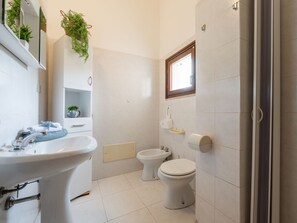 Un baño moderno con lavamanos, bidé, inodoro y un espejo con plantas.