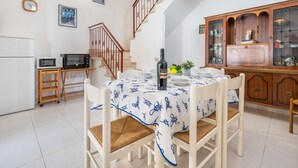 Zona pranzo con tavolo rotondo, sedie, una bottiglia di vino e una ciotola di frutta.
