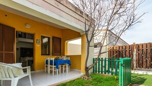 Una veranda con tavolo apparecchiato per mangiare, una sedia bianca e un piccolo giardino con un albero e una recinzione in legno.