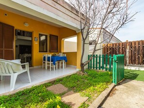 A patio with a table set for dining, a white chair, and a small garden area with a tree and a wooden fence.