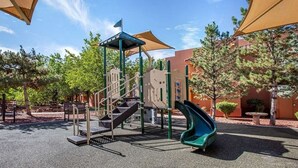 A playground with a slide and climbing structures, surrounded by trees and shaded by large umbrellas. - Sedona | Pool & Red Rocks | Canyon View Stay (Sedona)