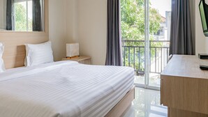 A hotel room with a large bed, a desk, a lamp, and a view of greenery through the window. - Collection O Kuta Near Airport Ngurah Rai (Tuban)