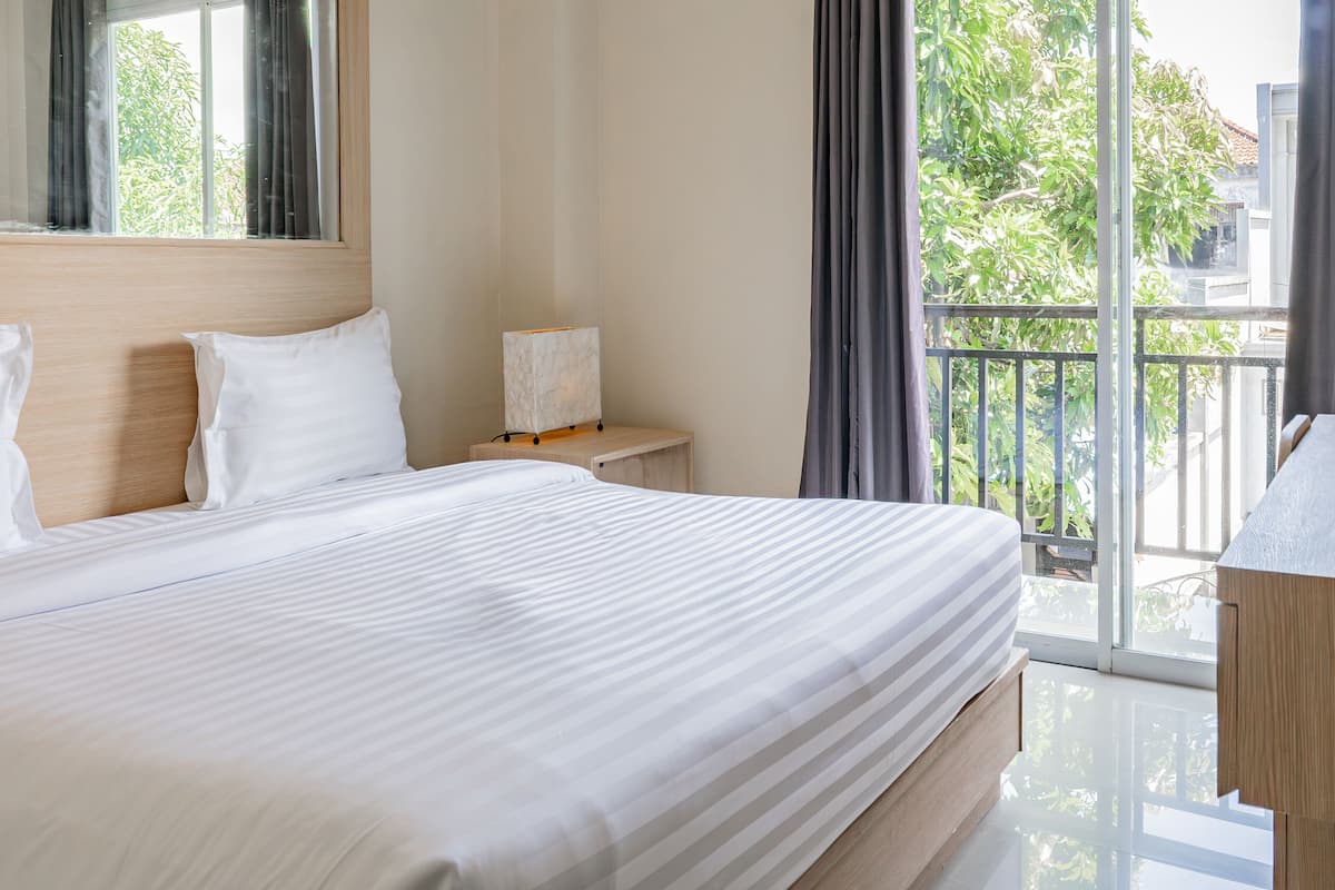 Une chambre d’hôtel avec un grand lit, un bureau, une lampe et une vue sur la verdure par la fenêtre.