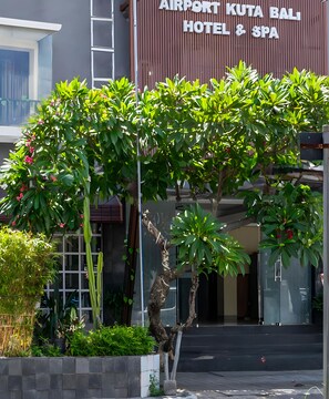 The exterior of Airport Kota Bali Hotel & Spa with a modern facade, a clear entrance, and lush greenery in front. - Collection O Kuta Near Airport Ngurah Rai (Tuban)