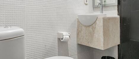 Baño con inodoro blanco, lavamanos y cubo de basura.