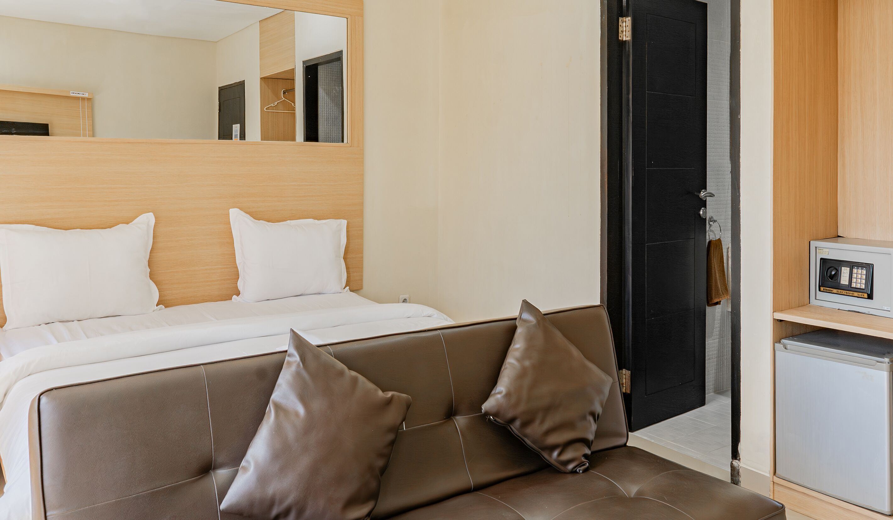 A hotel room with a bed, a sofa, a mirror, a door, and a small refrigerator.
