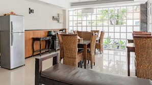 A modern kitchen with a refrigerator, wooden cabinets, and a dining area with wicker chairs and a bench. - Collection O Kuta Near Airport Ngurah Rai (Tuban)