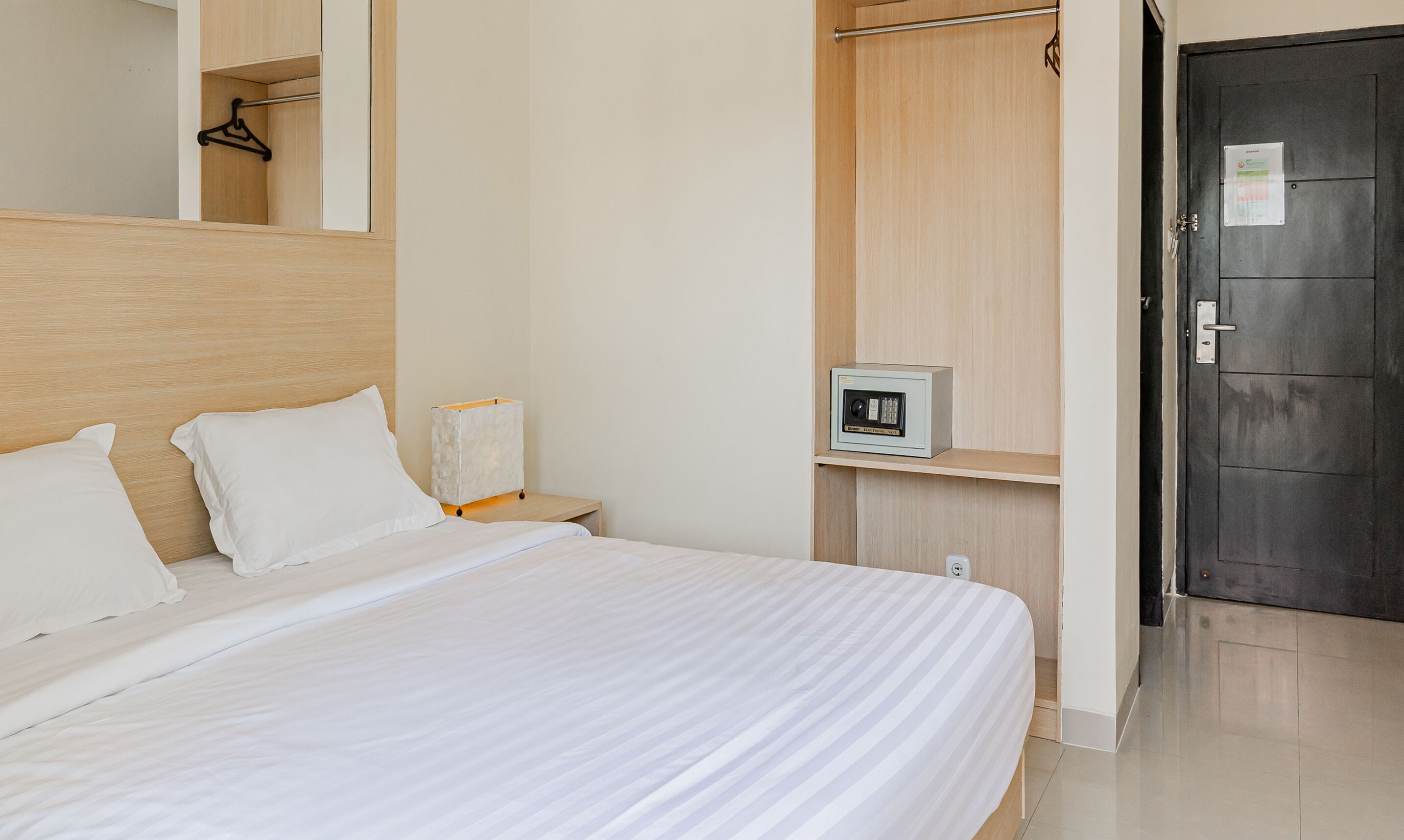 A hotel room with a bed, a bedside table, a wardrobe, and a safe.