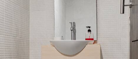 Un baño moderno con un lavabo blanco, tocador de madera y un espejo grande.