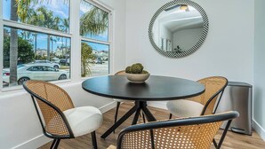 A dining area with a round table, four wicker chairs, a bowl with a plant, and a wall-mounted mirror. - Dahlia Suite I Steps to Bay, Shops, Food + More (Coronado)