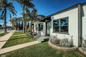 A modern building with a white exterior, large windows, and a well-maintained lawn with palm trees. - Dahlia Suite I Steps to Bay, Shops, Food + More (Coronado)