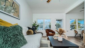 A modern living room with a sofa, a coffee table, and a dining area with chairs. - Dahlia Suite I Steps to Bay, Shops, Food + More (Coronado)