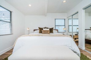 A modern bedroom with a large bed, white bedding, and a green rug. - Magnolia Suite I Steps to Shops, Dining + Bay (Coronado)
