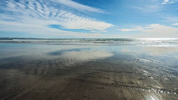 Una playa con arena húmeda y cielo despejado.