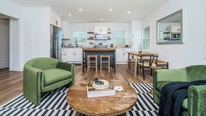 Una cocina moderna con gabinetes blancos, una isla central y un comedor con taburetes.