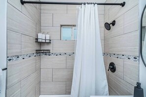 A modern bathroom with a shower curtain, a handheld showerhead, and a small window. - Magnolia Suite I Steps to Shops, Dining + Bay (Coronado)
