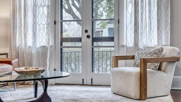 A living room with a glass coffee table, a cushioned armchair, and a view through a glass door.