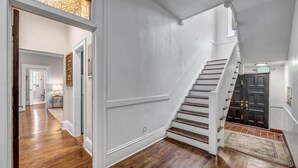 A hallway with wooden flooring, a staircase, and a black door.