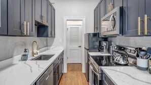A narrow kitchen with dark cabinets, a white countertop, and a stainless steel range hood.