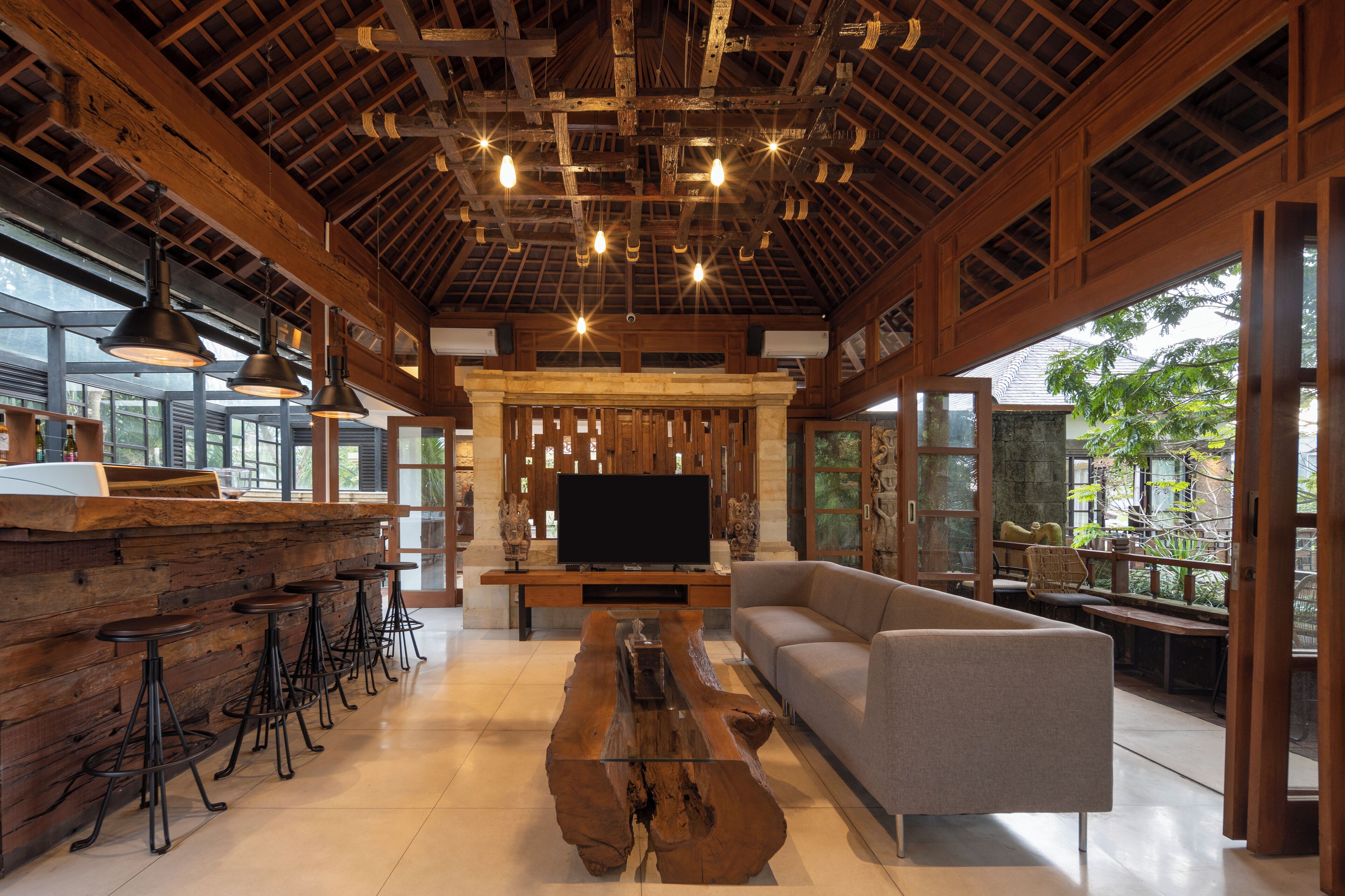A spacious room with a wooden ceiling, a large TV, a sofa, and a bar area with stools.
