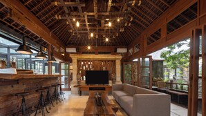 Une pièce spacieuse avec un plafond en bois, une grande télévision, un canapé et un coin bar avec des tabourets.